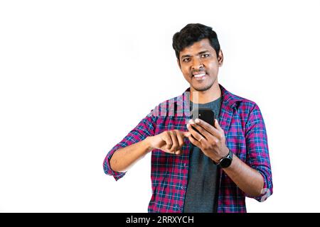A young man in his 20s looks up in surprise as he scrolls through his mobile phone. He is standing against a plain white background. Stock Photo