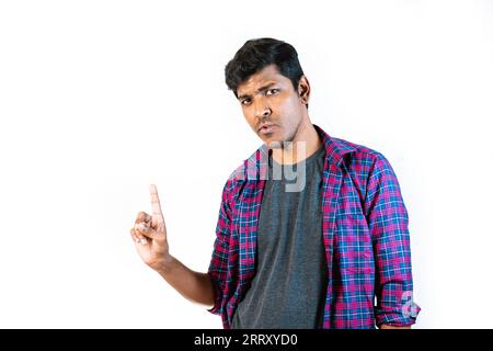 A young man with a surprised expression shakes his head in denial, looking directly at the camera. He is standing in front of a plain grey background. Stock Photo