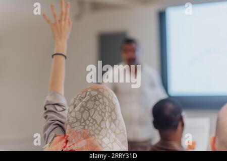 Back view photo of muslim woman raising hand to ask question Stock Photo