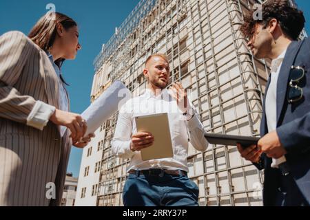Architects working outdoors, discussing project and blueprint on tablet Stock Photo