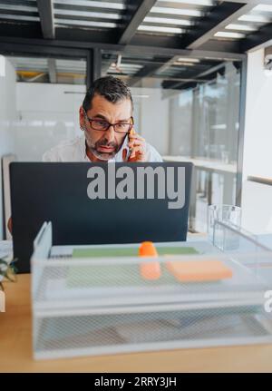 Senior or mature businessman having phone call while working on lap top at the office. Stock Photo