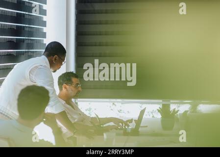 Diverse business professionals collaboratively discuss ideas in a green office, utilizing technology for efficient decision-making and strategic plann Stock Photo