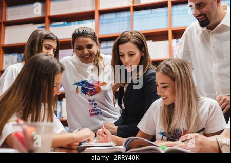 A group of students and professors collaborating and studying together in a library setting, working on a school project and sharing knowledge. Stock Photo