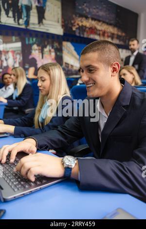 Young and well-dressed students smiling and working on their laptops in class Stock Photo