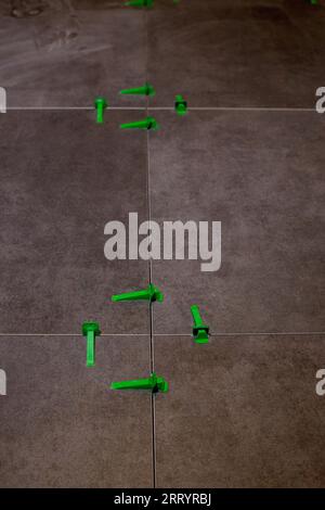 Tile levelling system, four plastic green clips with wedges. Close-up view, selective focus, blurred background. Stock Photo