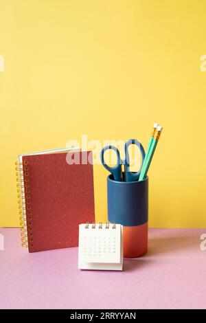 Notebook, pencil holder, calender on pink desk. yellow background. workspace Stock Photo