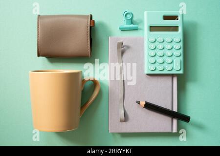 Notebook, calculator, clip, mug cup, pouch on green desk background. flat lay, top view. workspace Stock Photo