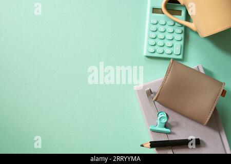 Notebook, calculator, clip, mug cup, pouch on green desk background. flat lay, top view. workspace Stock Photo