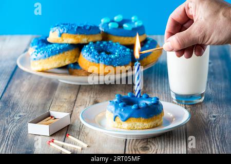 A hand lighting a candle on a blue chocolate candy dipped donut. Stock Photo