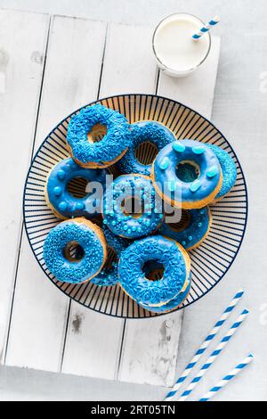 A pile of blue chocolate dipped donuts on a plate with a glass of milk. Stock Photo