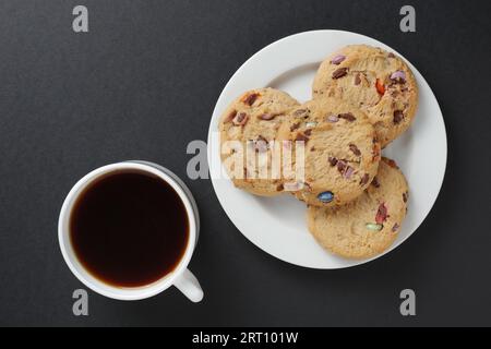 Cookies with colored chocolate sweets and cup of coffee on wooden background. Top view Stock Photo