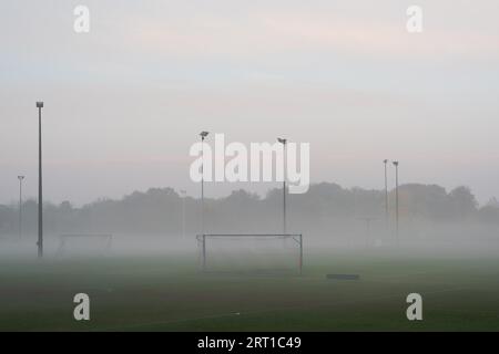 Empty and deserted soccer field in suburban area with goals and flood light poles on grey overcast day with fog and mist Stock Photo