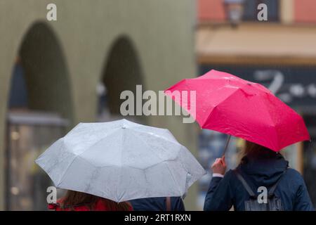 Upper body parts of two unrecognizable people with rain umbrellas walking through street in old narrow shooping street on rainy day Stock Photo