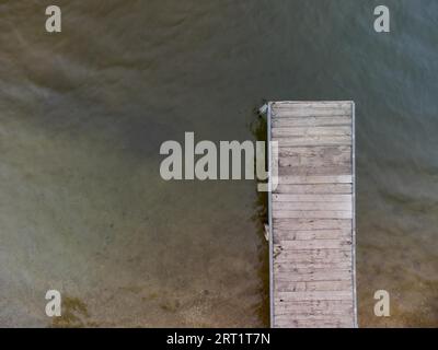 Aerial top down drone shot of wooden pier for swimmers and boats leading into swimming lake of local recreation area Stock Photo