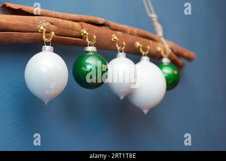 White and green christmas ornament balls hanging on hooks on big cinnamon stick on cord against blue painted wall Stock Photo