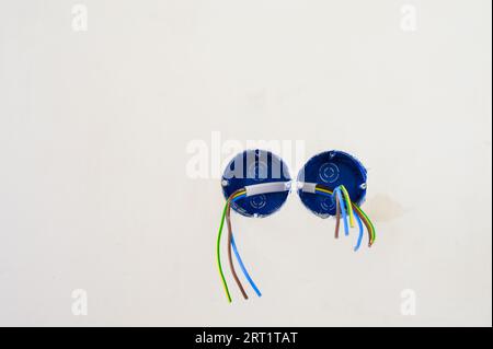 Preparing to install the socket in the wall. Electrical wires sticking out from electrical socket hole on gray concrete wall. Stock Photo