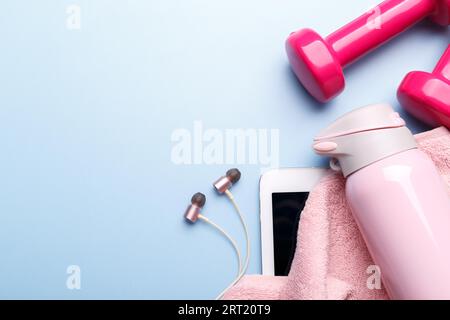 Fitness concept flat lay on blue background with sneakers, dumbbells and measuring tape, pink towel and water bottle, flat lay copy space Stock Photo