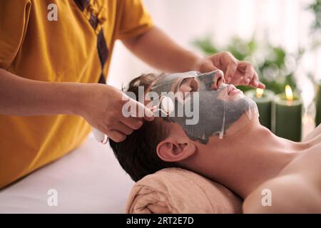 Cosmetologist giving rejuvenating face massage to man after applying face mask Stock Photo