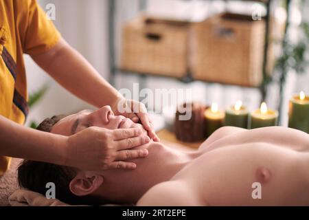 Beautician giving young man rejuvenating face massage to reduce appearance of wrinkles and fine lines. Stock Photo
