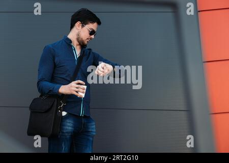 Young corporate businessman in casual wear looking at his wristwatch Stock Photo