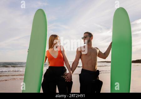 Young Surfers Couple Holding Hands And Posing With Surfboards On The Beach Stock Photo