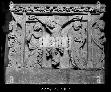 Church Of The Holy Rood, Shilton, West Oxfordshire, Oxfordshire, England, 1940-1949. Detail of a panel in a 15th century square font in Holy Rood Church.Detail of a panel showing the Crucifixtion of Christ. The figure of Christ is on the cross in the centre of the panel, with a woman stood on his right, possibly Mary, and a man holding a book on his left. The scene is bordered with vertical supports and there is a robed figure stood on each corner of the font. Stock Photo