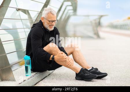 Elderly sportsman jogging by bridge, suffering from shin splint Stock Photo