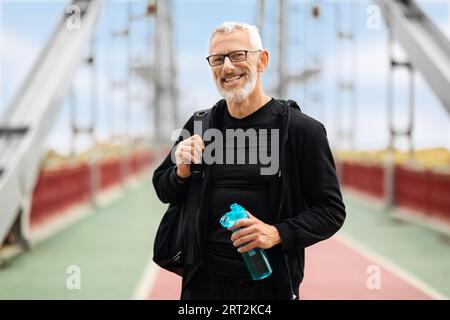 Positive retired sportsman standing on walking bridge, going home Stock Photo