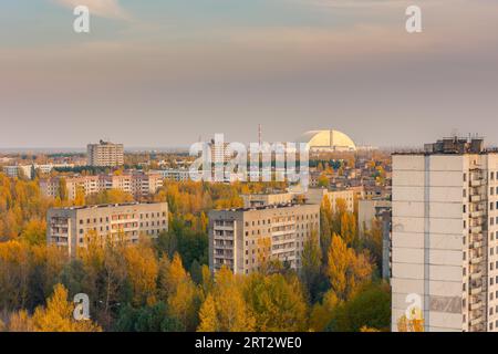 Aerial view from the top of an abandoned apartment skyscraper in Pripyat, Chernobyl Exclusion Zone with the exploded reactor block 4, covered by the Stock Photo