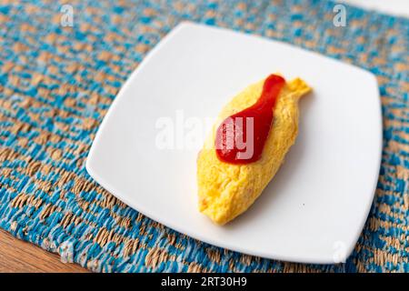 A close-up view of a delicious golden yellow omelet. Topped with a little ketchup. Placed on a white plate with a fabric-patterned cloth. The copy are Stock Photo