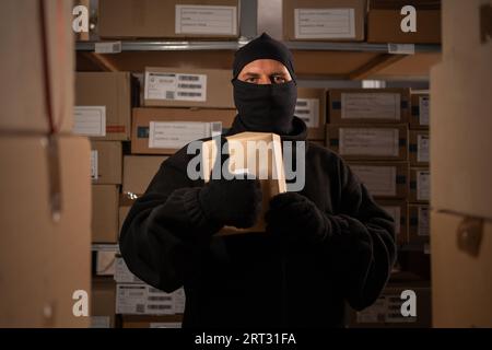 Adult male thief an in a ski mask picks up a box with a parcel in a