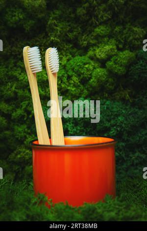 Bamboo toothbrushes in an orange glass on a natural background. Wooden ecological toothbrushes. Stock Photo