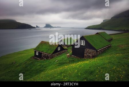 Tradicional faroese grass - covered houses in the village Bour. Drangarnir and Tindholmur sea stacks on background. Vagar island, Faroe Islands, Denma Stock Photo