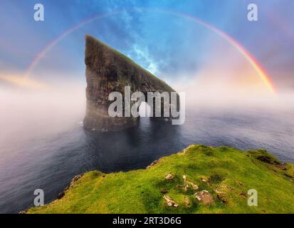 Rainbow over coast cliff in ocean Drangarnir in Faroe island. Sunset landscape Stock Photo