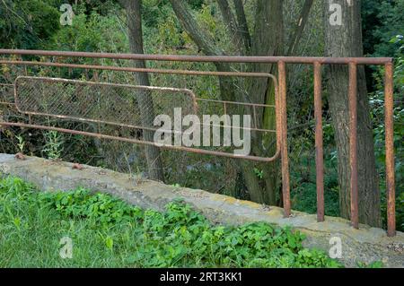 An old rusty fence on a concrete base in the green woods Stock Photo