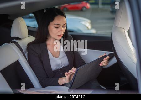 Young businesswoman using digital tablet while sitting in the back seat of a car. Copy space. Business, road trip, technology, travel concept Stock Photo