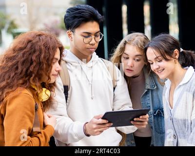 Group of teenage students brainstorm on a campus while looking at a tablet. Students work in teams Stock Photo