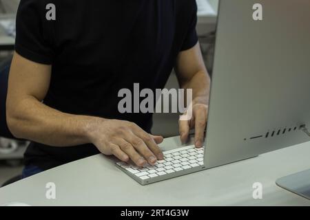 Young man in a black T-shirt working with computer, man's hands on keyboard computer Stock Photo