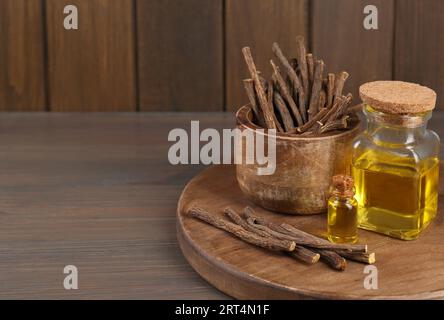 Dried sticks of licorice roots and essential oil on wooden table. Space for text Stock Photo