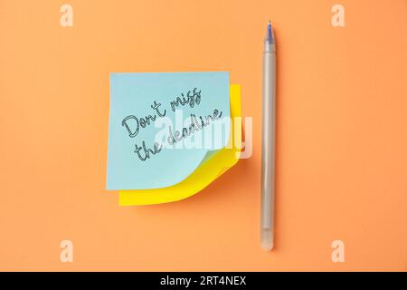 Note with reminder Don't Miss The Deadline and pen on orange background, top view Stock Photo