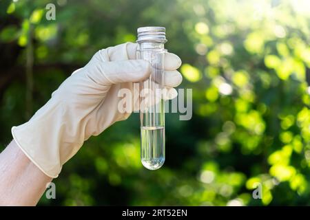 Scientist is holding in hands a clear and dirty water test tubes close up on blurry green background of nature... Stock Photo