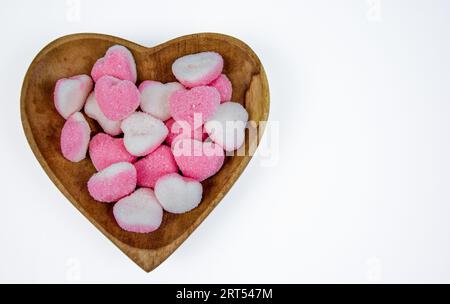 pile of heart shaped sugar Candies on a heart shaped wooden bowl isolated on a white background Stock Photo