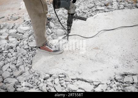 Worker use Electric Concrete Breaker. Worker destroy surface with jackhammer, drilling concrete construction works. Stock Photo
