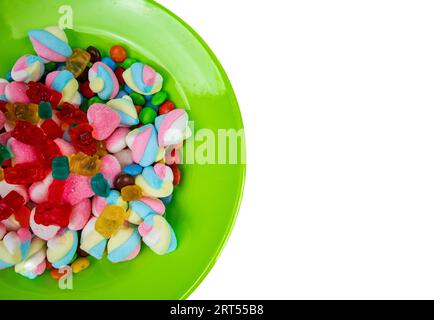 piles of various kinds of sweets and candies. Milk chocolate candy and jelly gum on a green plate isolated on white background, top view Stock Photo