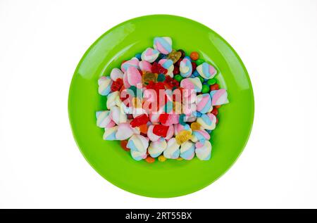 piles of various kinds of sweets and candies. Milk chocolate candy and jelly gum on a green plate isolated on white background, top view Stock Photo