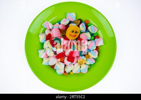 piles of various kinds of sweets and candies. Milk chocolate candy and jelly gum on a green plate isolated on white background, top view Stock Photo