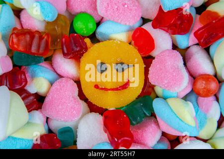 piles of various kinds of sweets and candies with a focus on the smiling candy Stock Photo