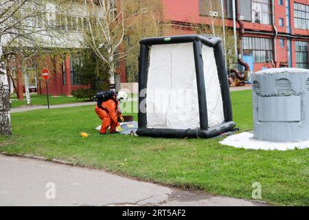 A professional firefighter in an orange special fireproof suit prepares to assemble a white oxygen tent to rescue people at a chemical, oil refinery, Stock Photo