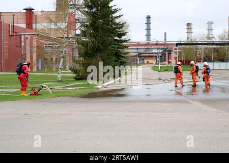 Professional firefighters in orange fire-resistant suits in white helmets with gas masks are testing fire hoses and fire guns to extinguish a fire at Stock Photo