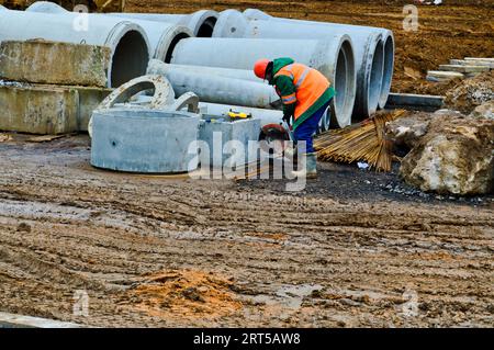 A builder worker in a helmet and a robe works with an industrial iron saw grinder at a construction site with an industrial saw. Stock Photo